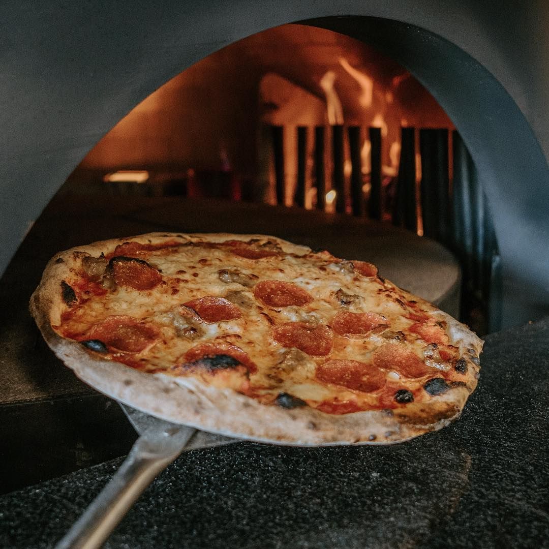 A pepperoni pizza is being taken out of a pizza oven