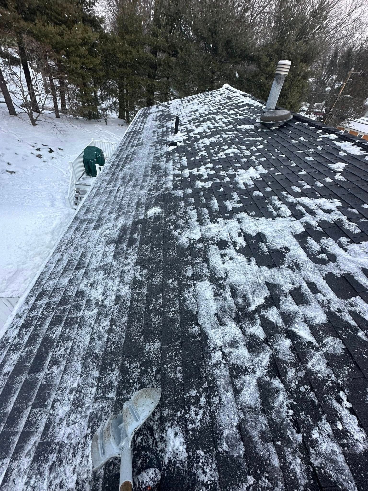 Snow-covered roof with a person shoveling snow. Winter scene in a forested area.
