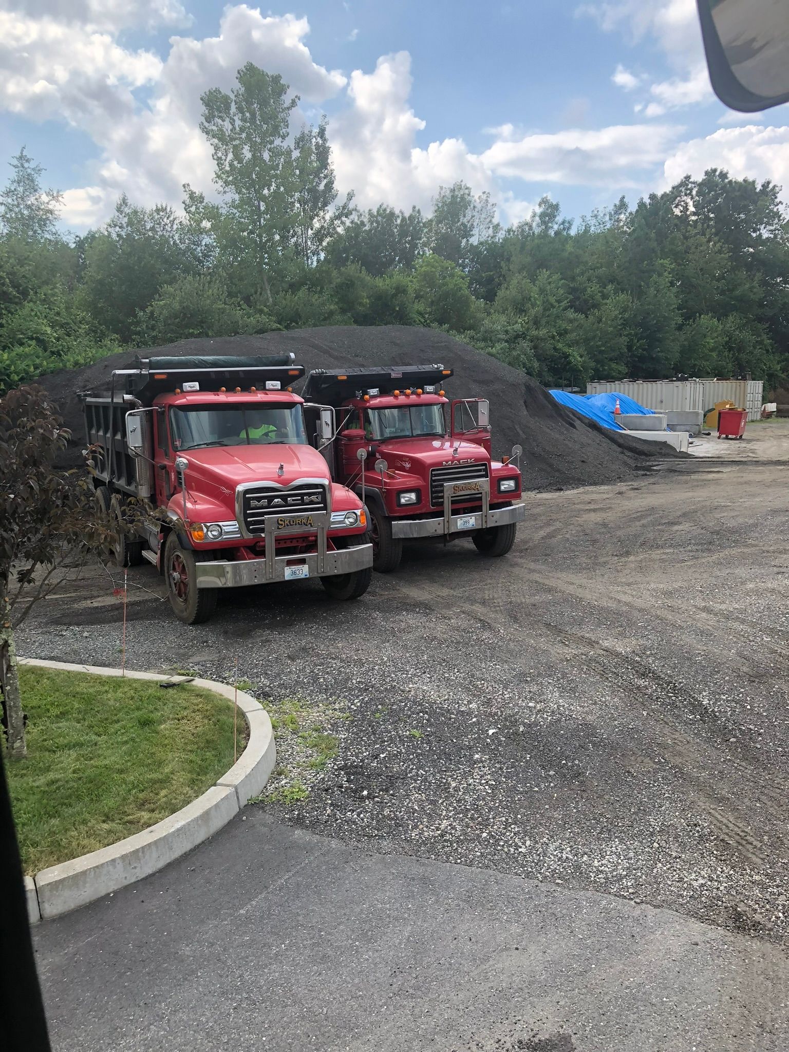 Two red dump trucks are parked next to each other in a gravel lot