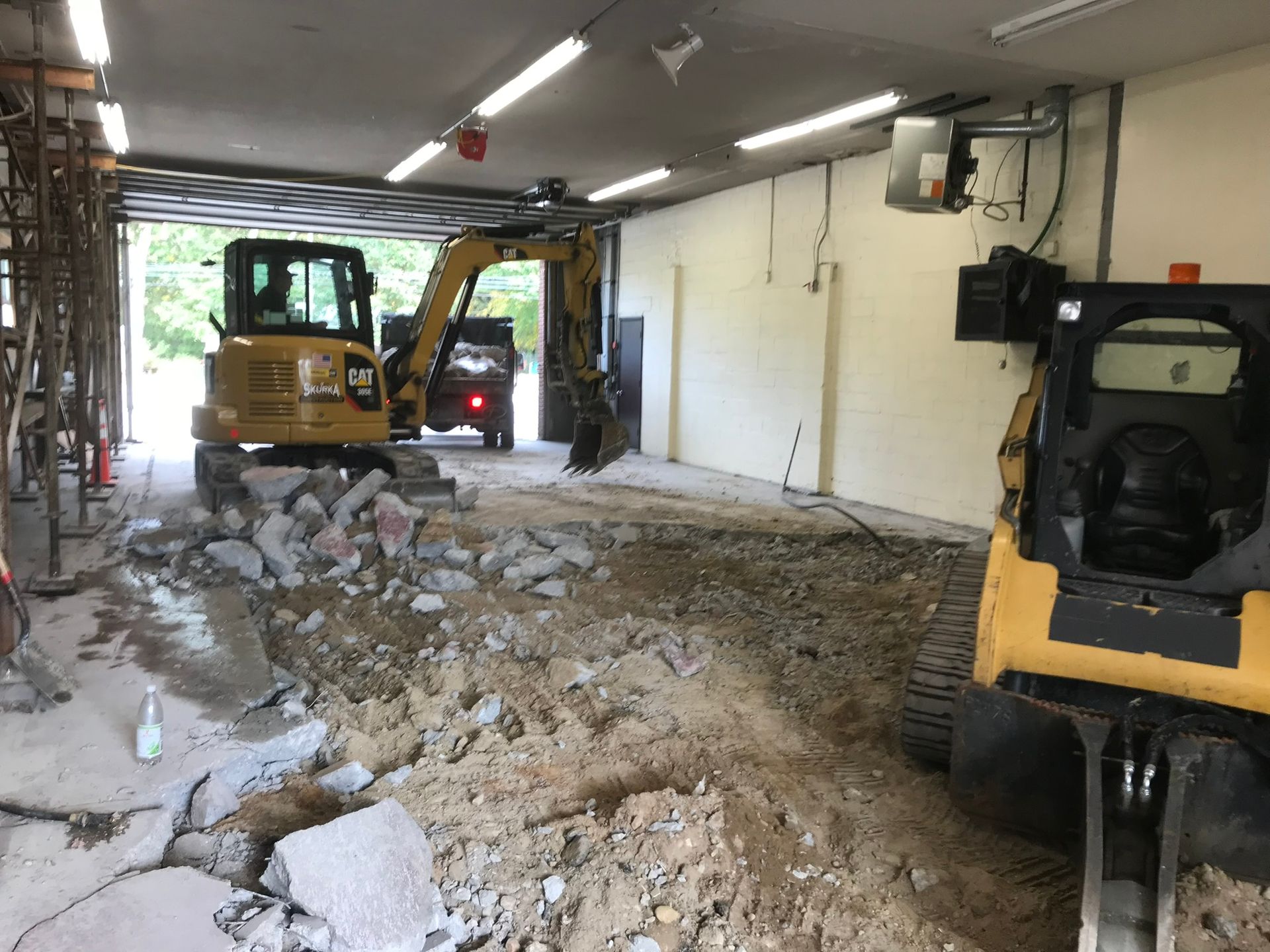 A yellow excavator is breaking concrete in a garage
