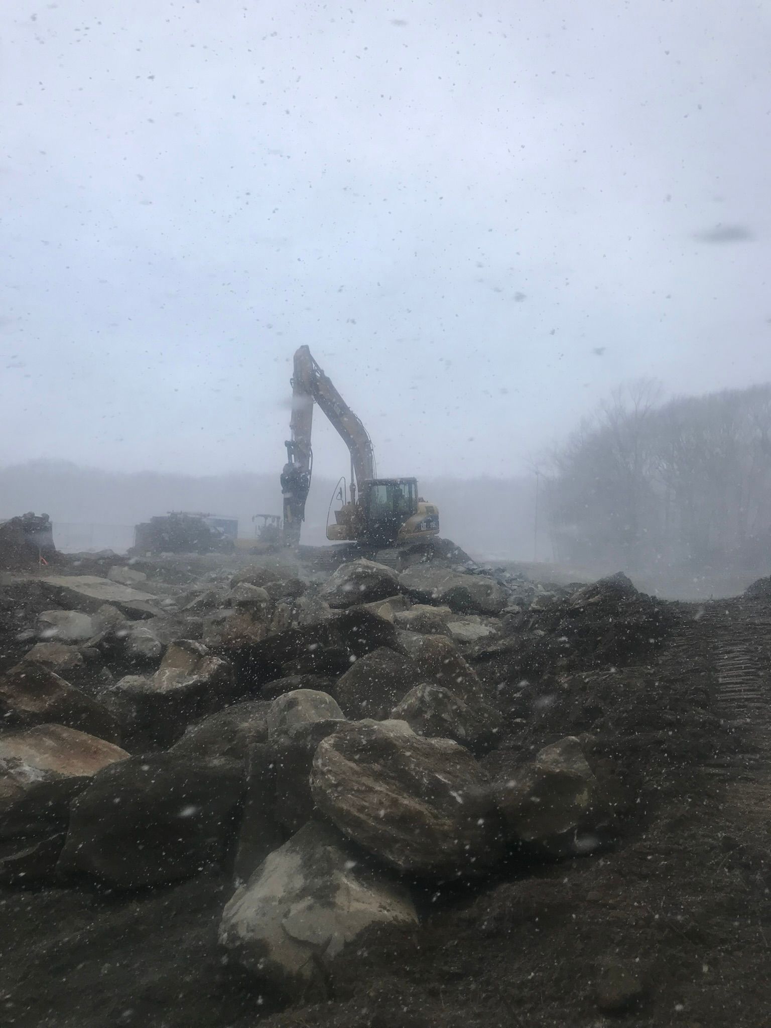 A large excavator is working on a pile of rocks in the snow