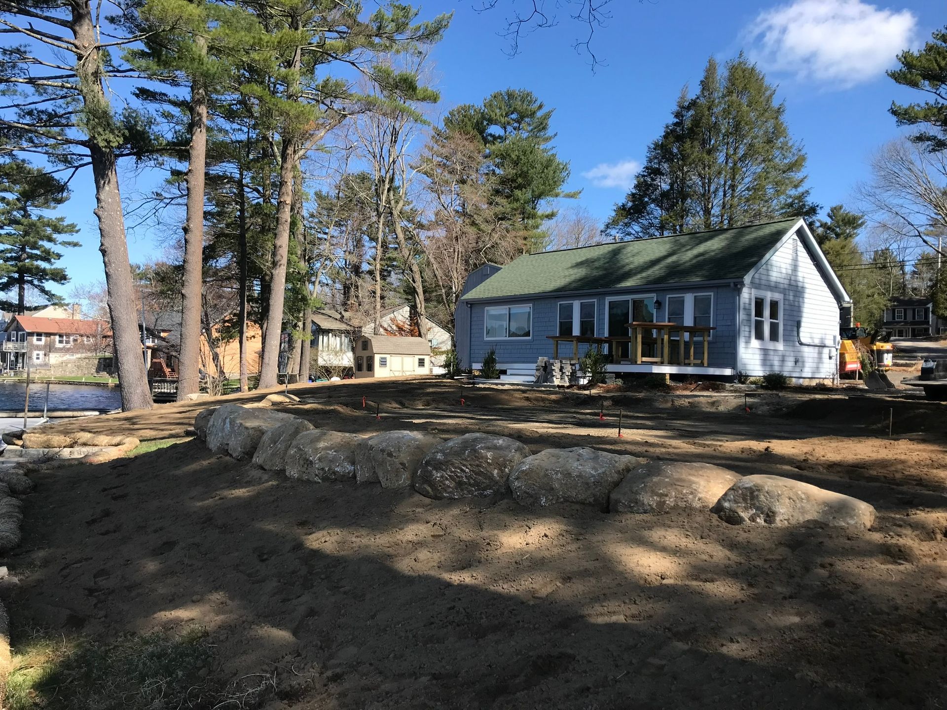 A white house with a green roof is surrounded by trees and rocks