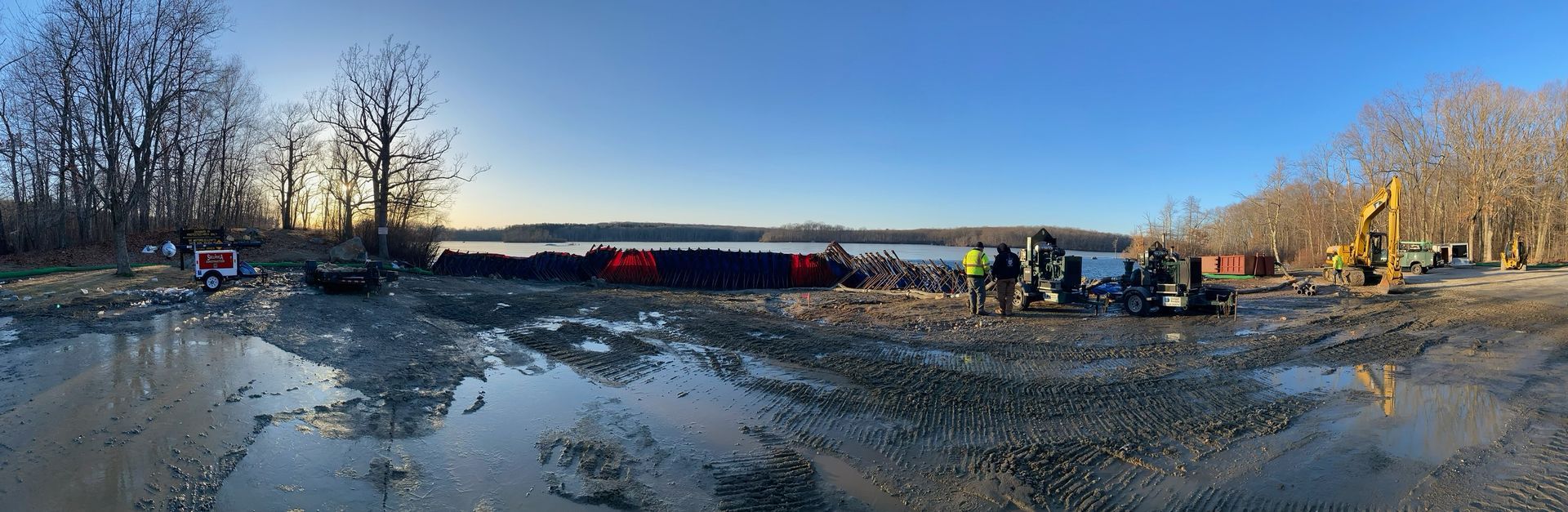 A group of people are standing in a muddy area near a body of water