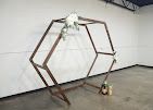 Geometric metal sculpture in a gallery, with a person standing beside it for scale.
