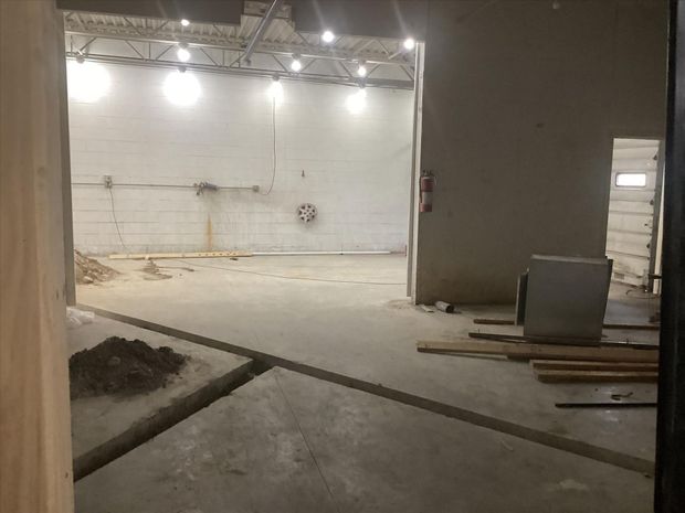 Empty indoor construction area with concrete floor, unfinished walls, and scattered materials under bright lights