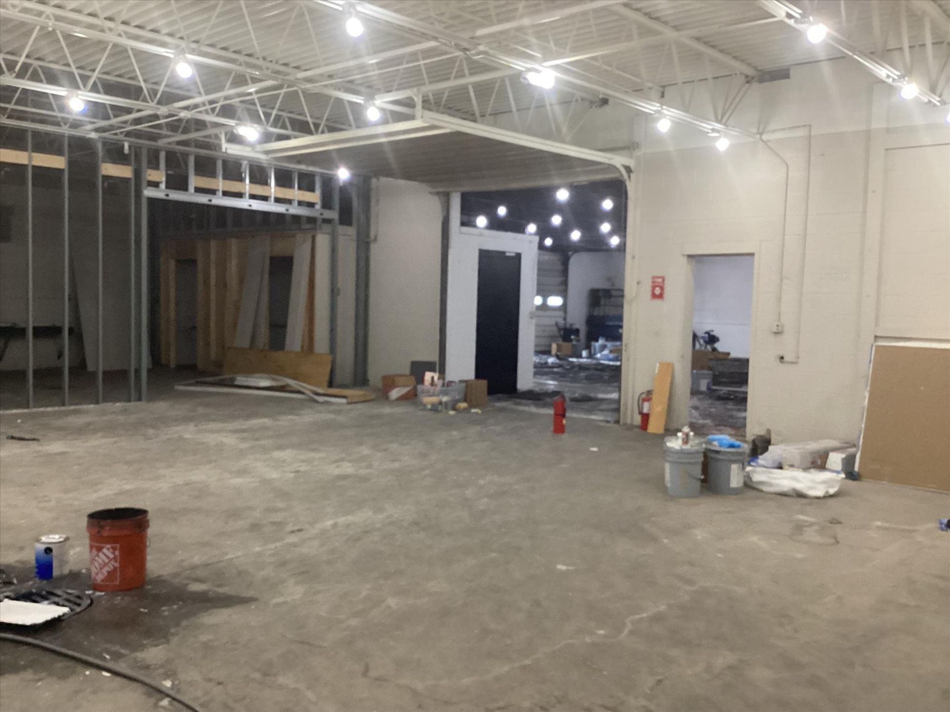 Empty warehouse interior under construction with exposed ceiling, open walls, and scattered tools and materials