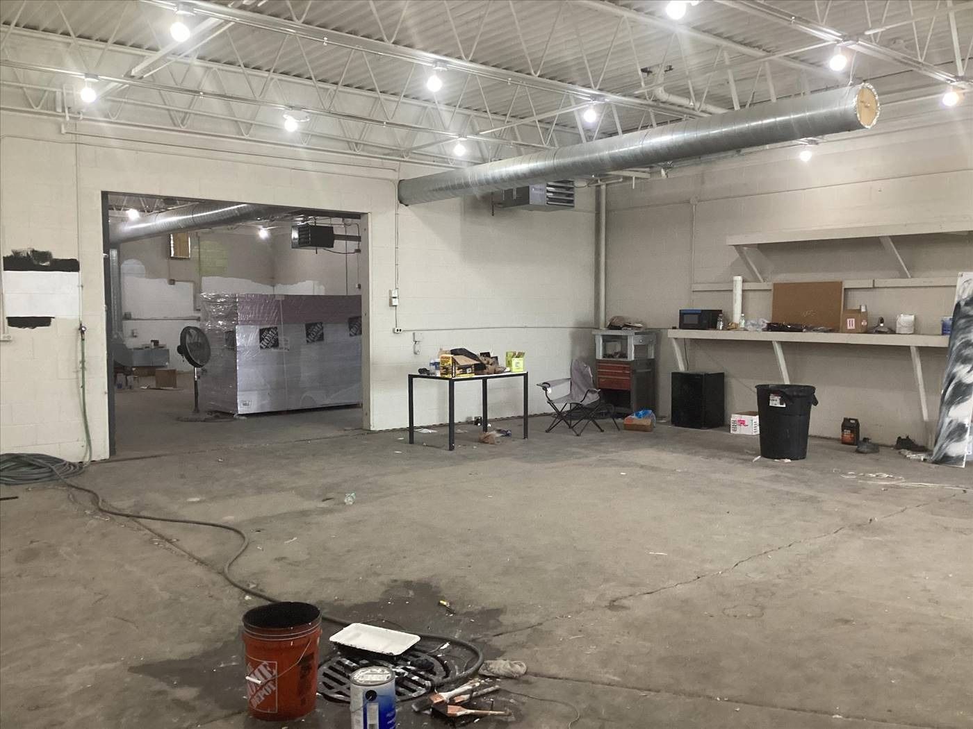 Empty industrial garage with concrete floor, workbench, shelves, and scattered tools under bright overhead lights