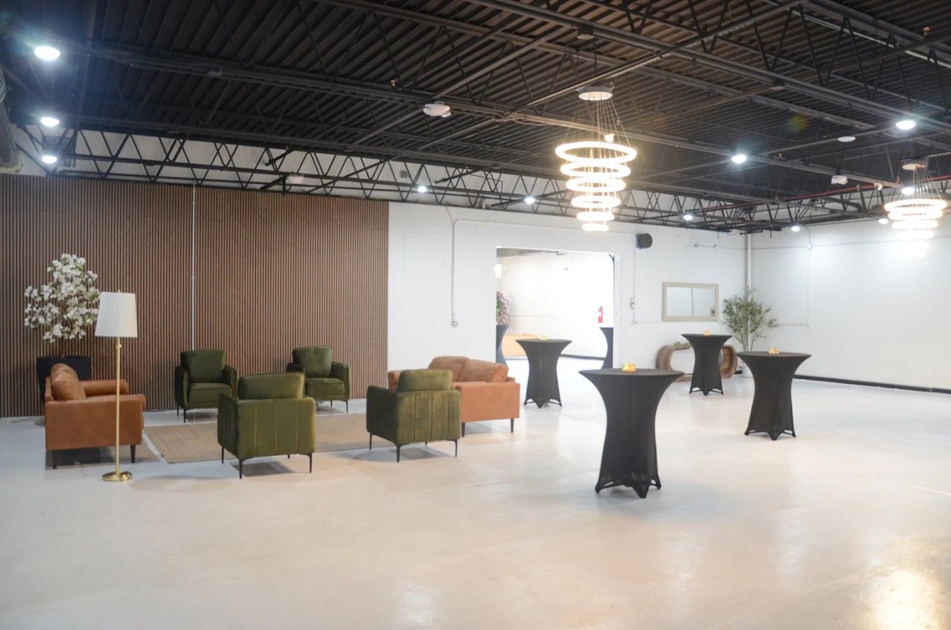 Empty event space with lounge chairs, cocktail tables, and modern hanging lights under an industrial ceiling