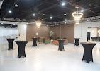 Empty banquet hall with white floor, black cocktail tables, chandeliers, and warm wall lighting