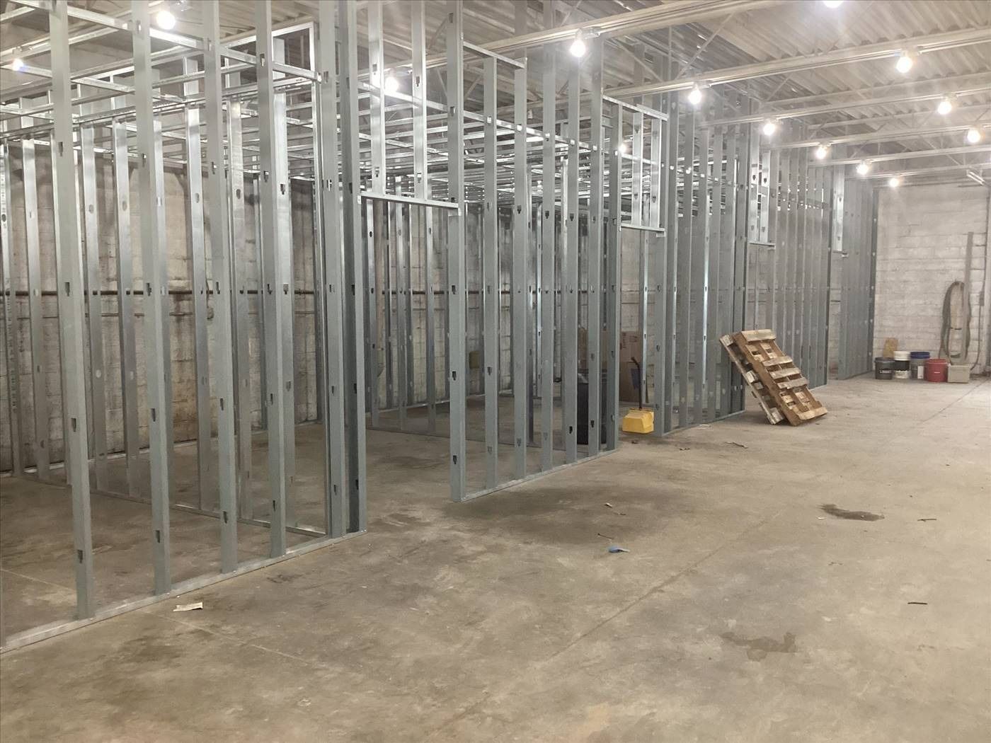 Interior of an unfinished building with exposed metal framing, concrete floor, and construction materials stacked near the wall.