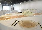 Elegant banquet table set with gold plates and white floral centerpiece in a bright event hall
