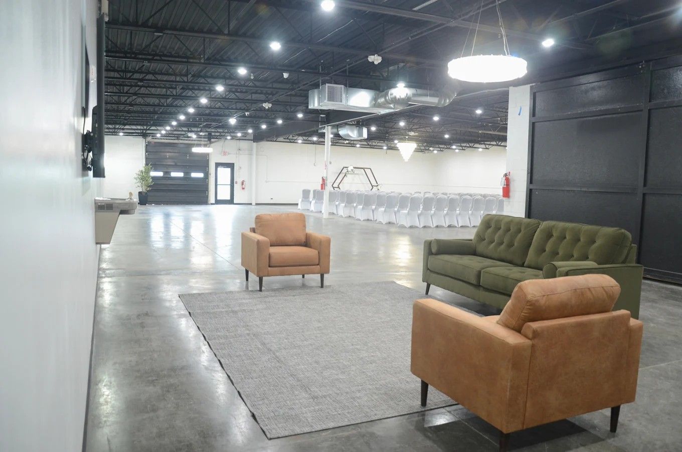 Modern industrial lounge with tan armchairs, green sofa, and gray rug in a large open space