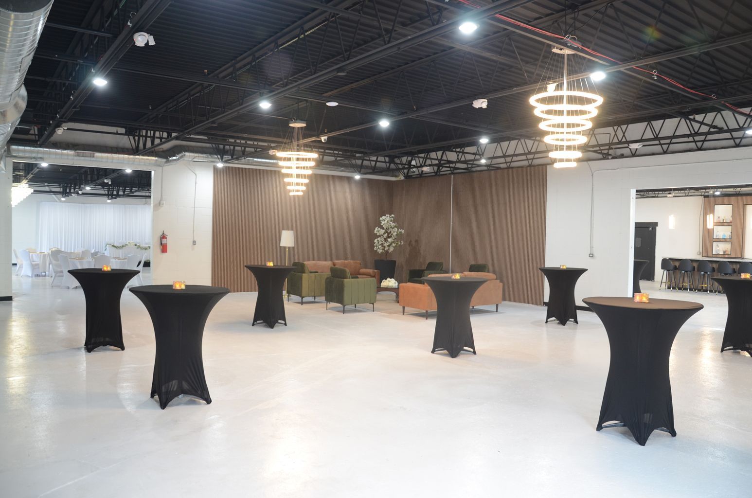 Spacious event hall with black cocktail tables, white floor, and warm pendant lights.