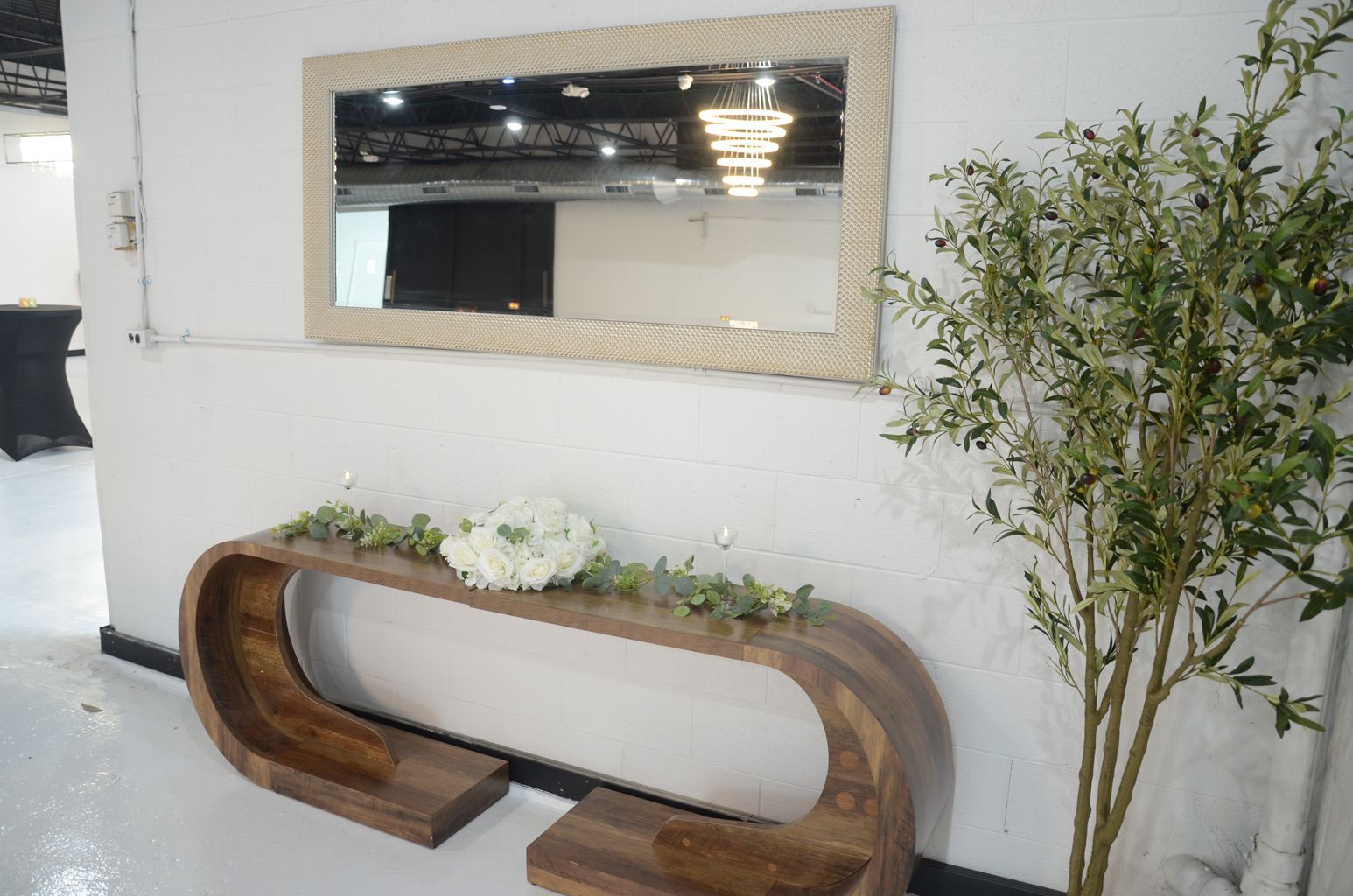 Modern lobby wall with mirror, wooden bench, white flowers, and potted tree