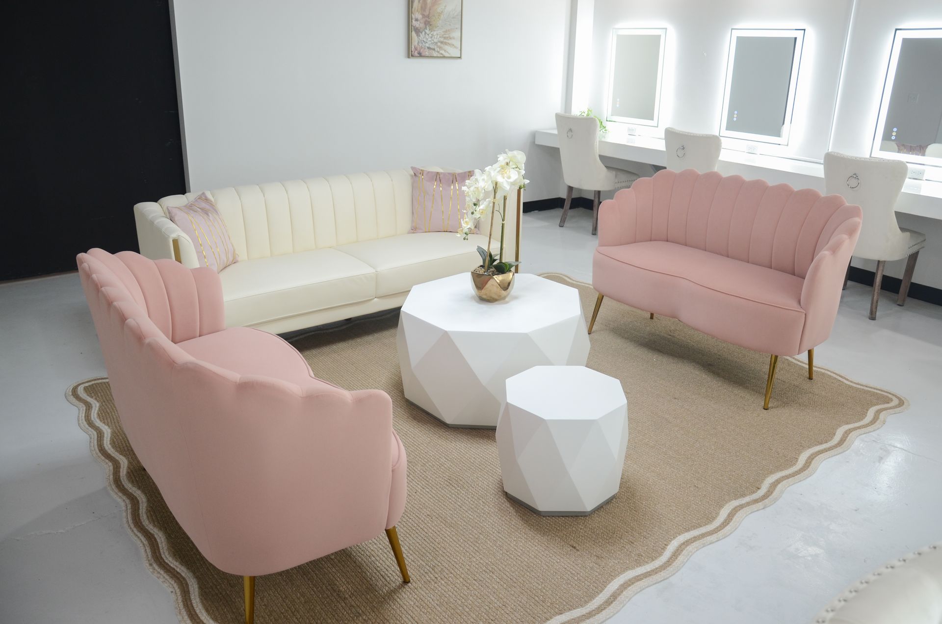 Pastel lounge with pink sofas, cream loveseat, white tables, and a floral centerpiece on a rug