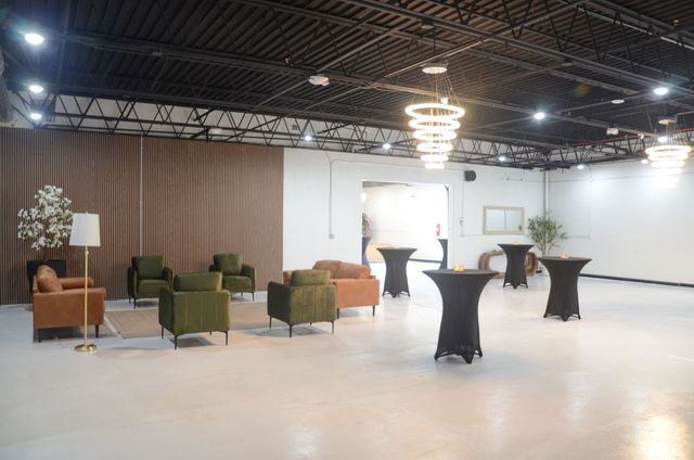 Spacious event hall with cocktail tables, green chairs, and a central chandelier under an exposed black ceiling