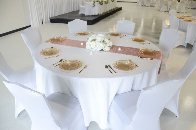 Round banquet table with white linen, gold place settings, and white chair covers in a bright event hall