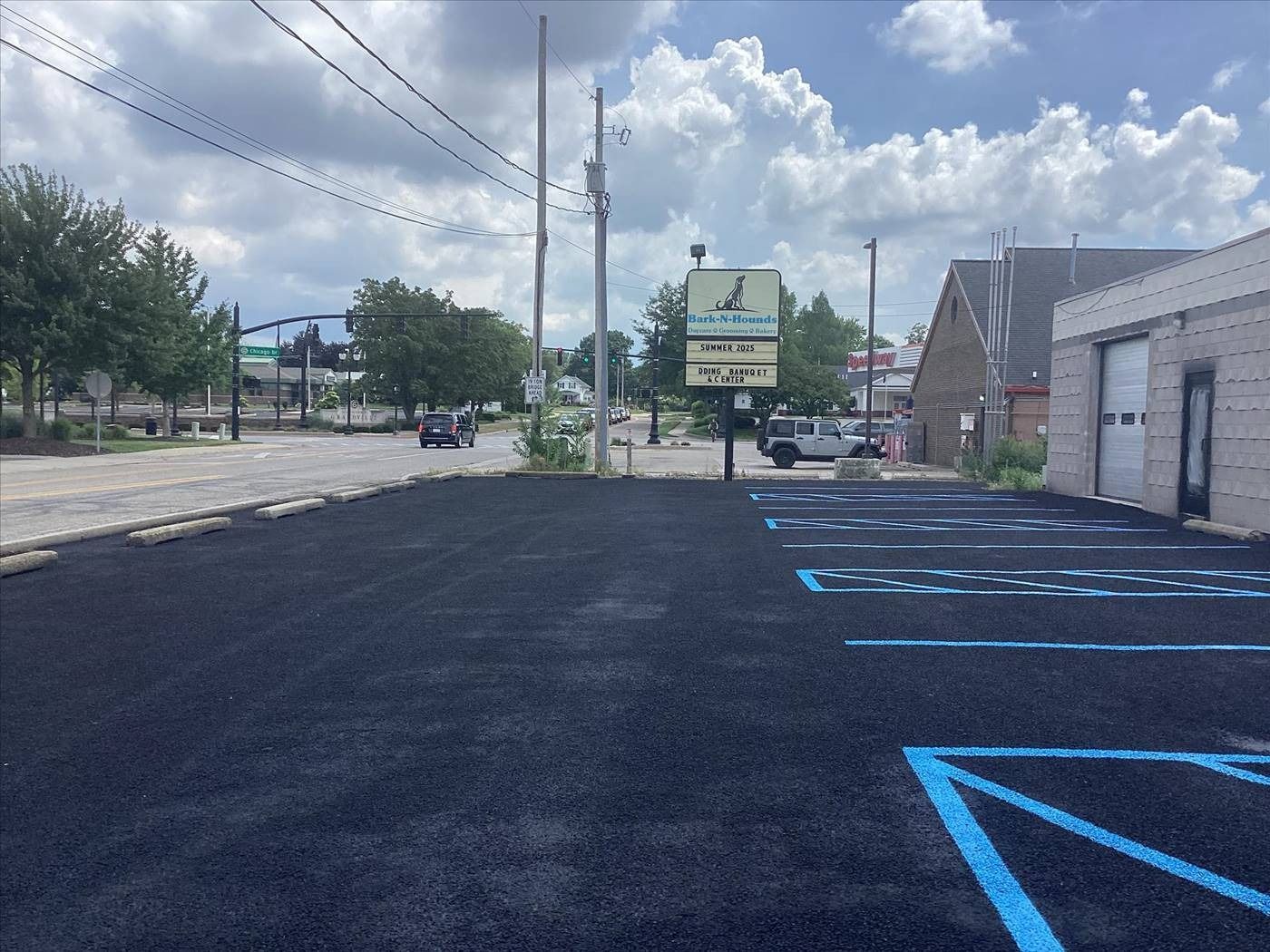 Freshly paved parking lot with blue-striped accessible spaces beside a small building under cloudy skies