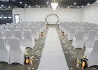 White wedding ceremony aisle lined with chairs and floral decorations, facing a hexagonal arch at the altar