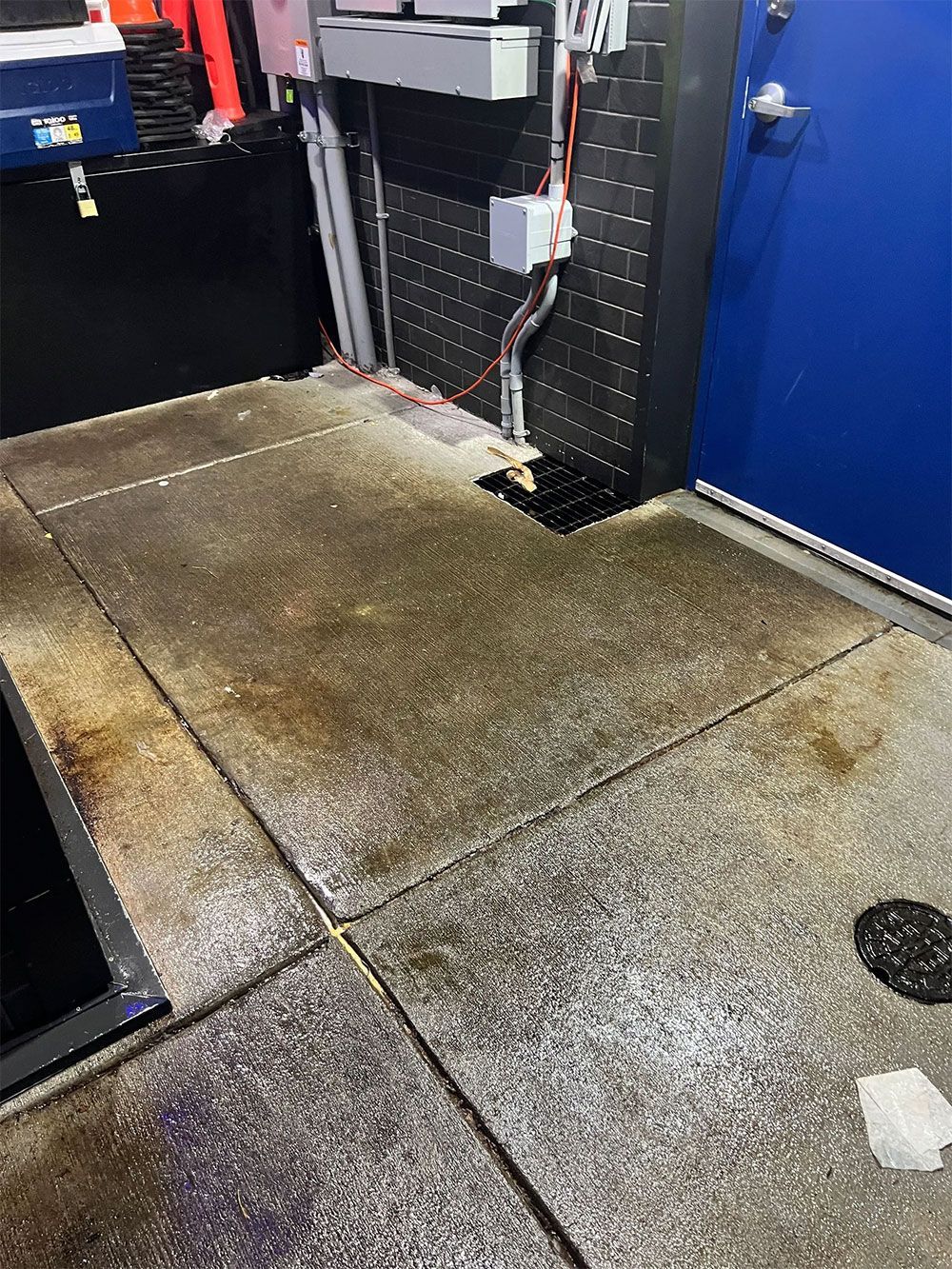 Wet concrete floor with visible drain and electrical panel, likely in a car wash bay.