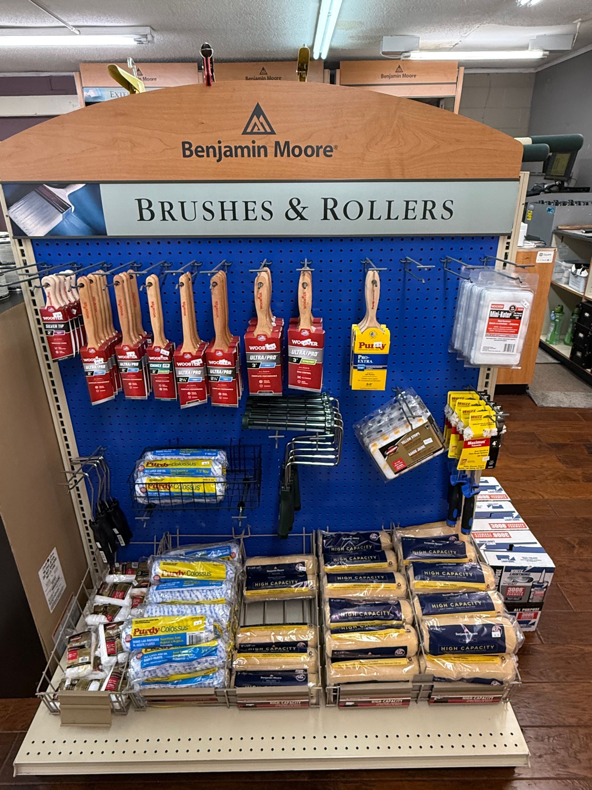 Benjamin Moore paint brushes and rollers on a store display with blue backing and beige shelving.