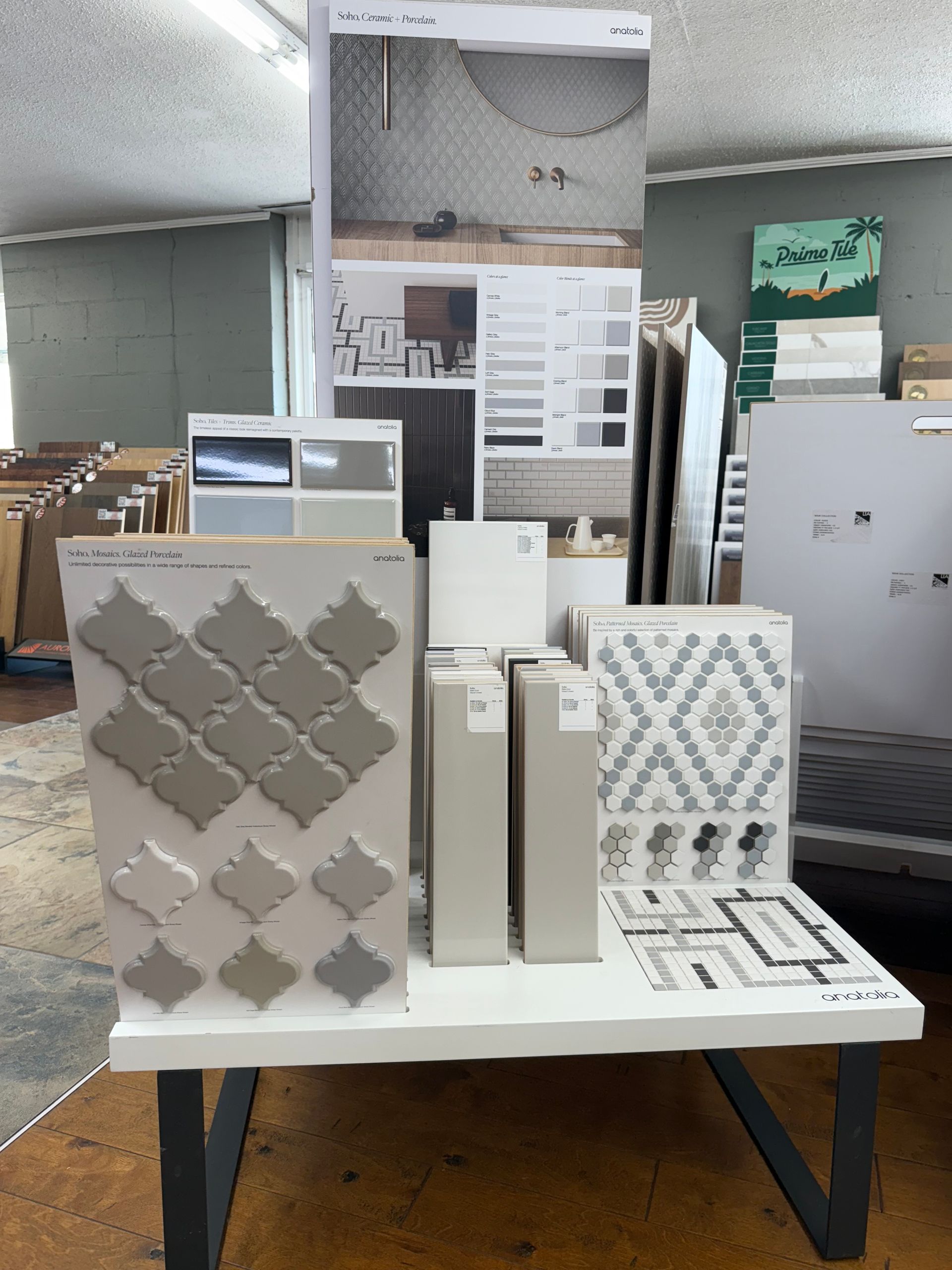 Display of various tiles on a white table, featuring grey, beige, and patterned designs.