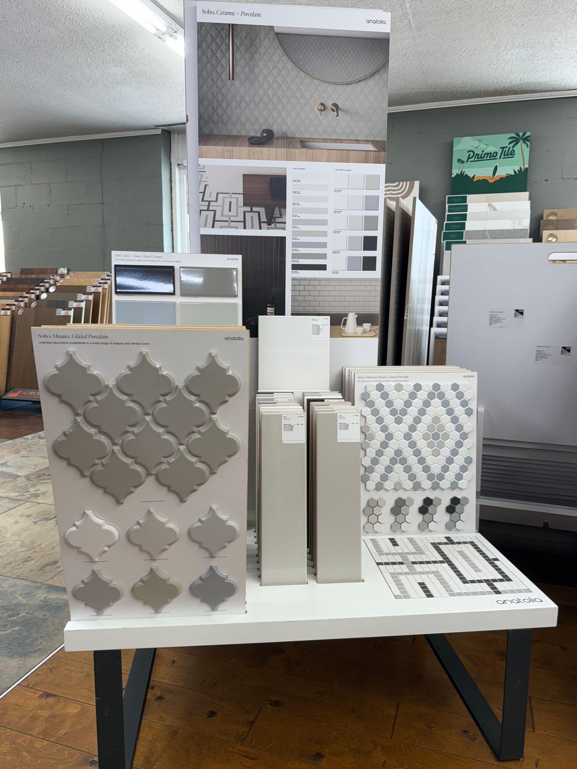 Display of various tiles in a store, showcasing different colors, shapes, and patterns on a white table.
