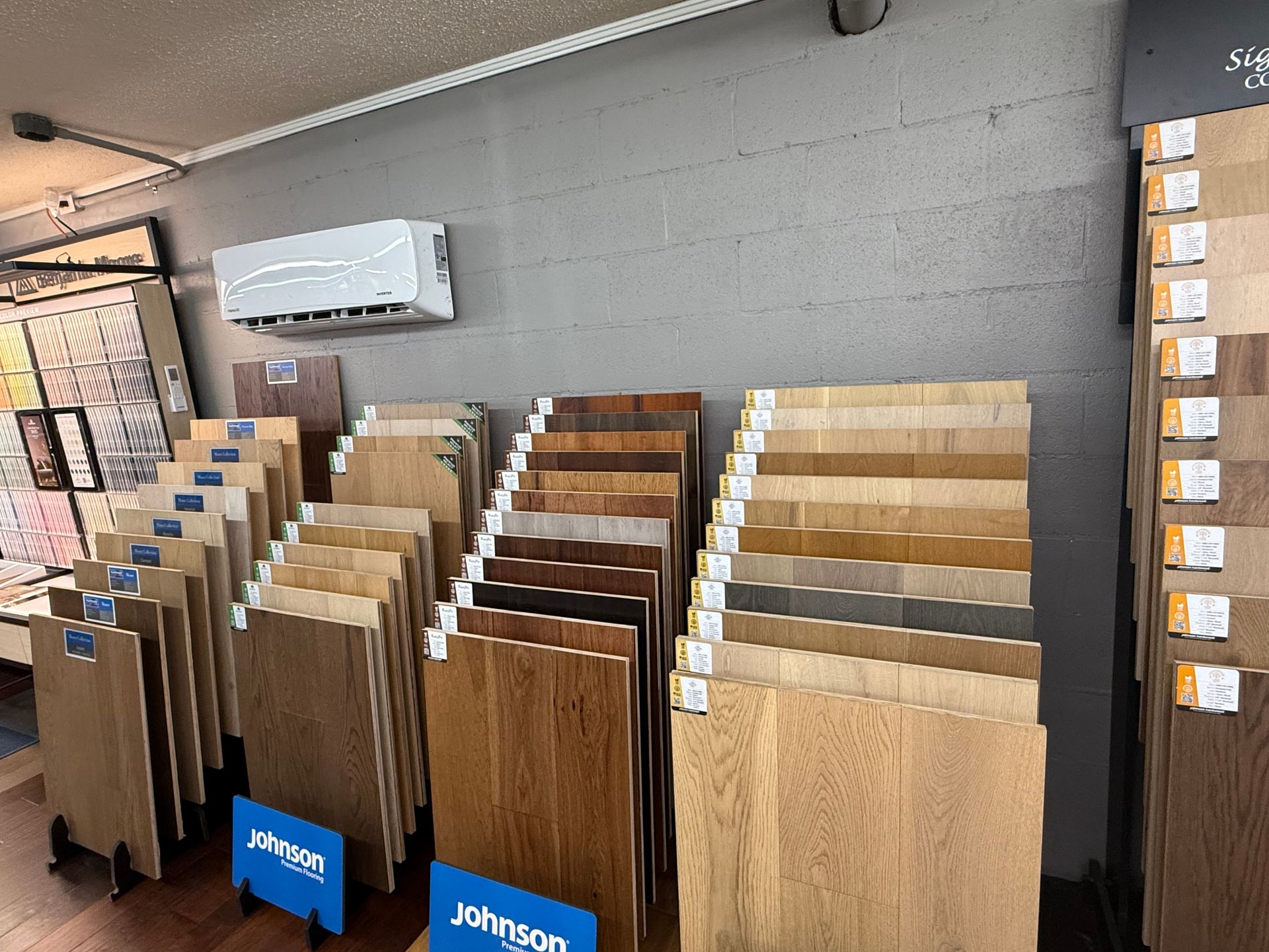 Rows of wood flooring samples on display in a showroom with an air conditioner mounted on the wall.