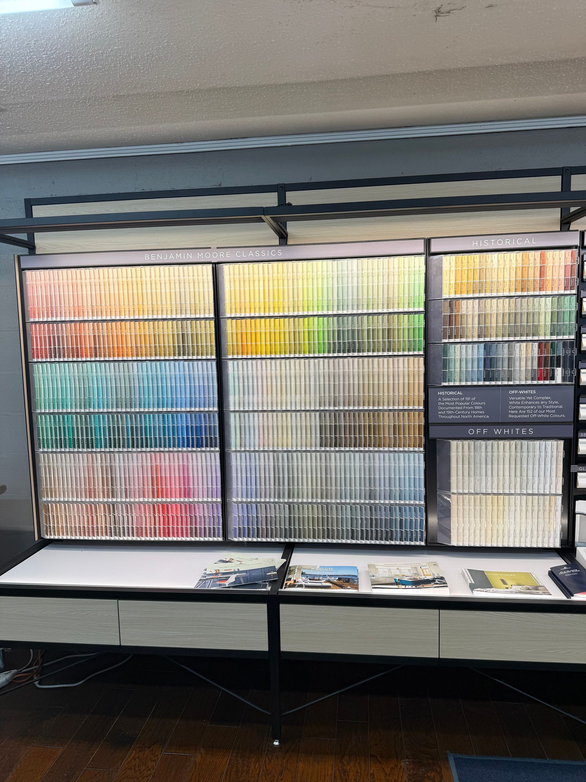Paint color sample display with rows of various hues, arranged by color family, in a store setting.