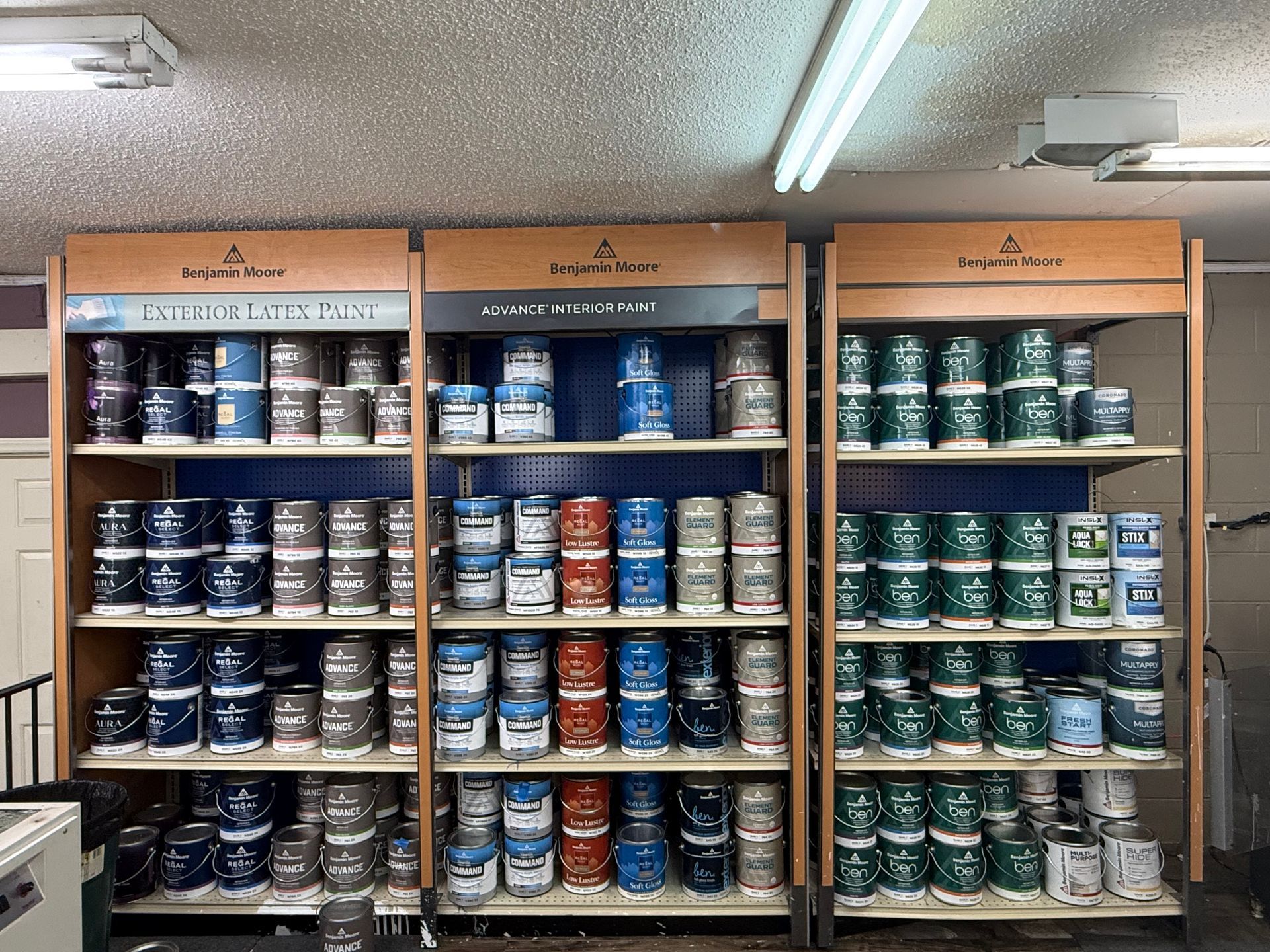 Paint cans displayed on shelves in a store. Colors range from blue and red to green.