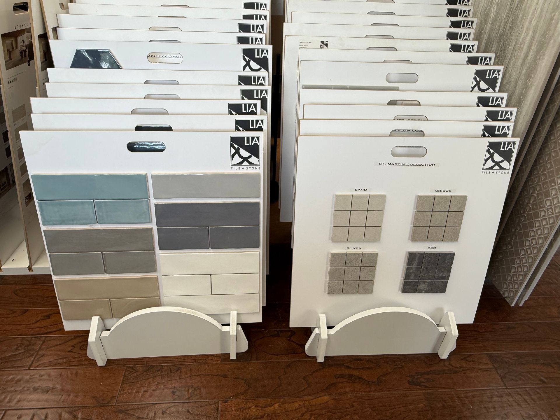 Tile samples on display, arranged on white stands. Various colors and textures, including blue, gray, and beige brick styles.
