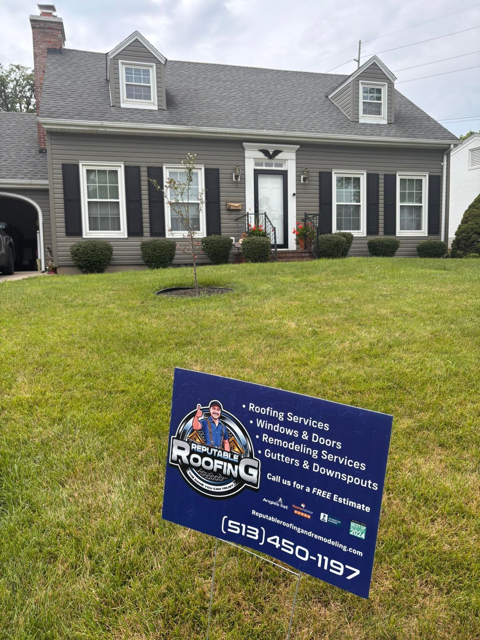 A house with gray siding and roof, black shutters, and a sign in the yard that says 