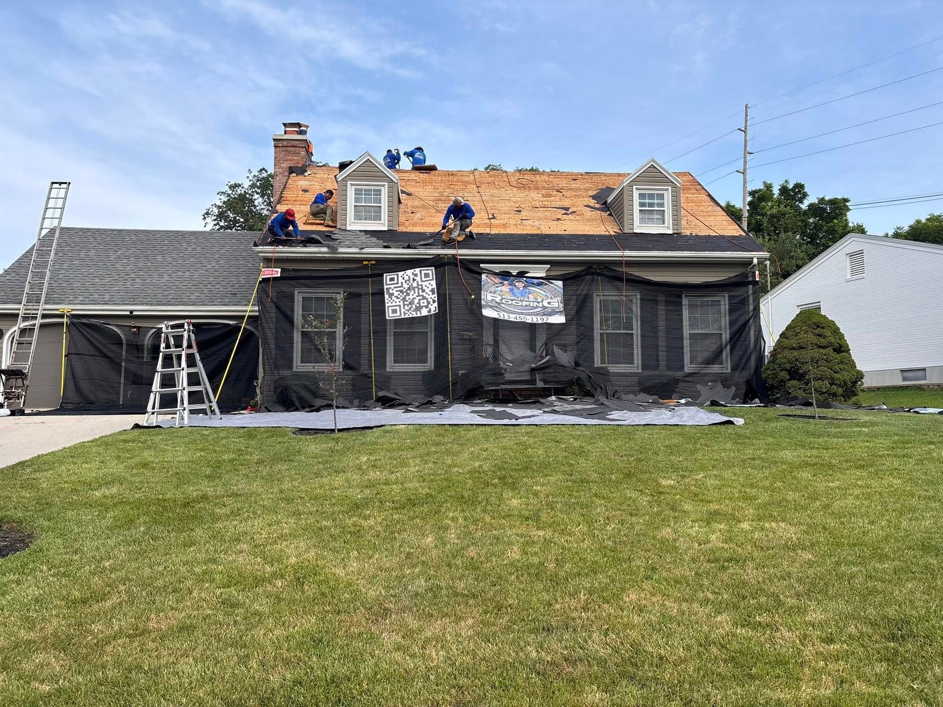 House with roof being replaced; workers on roof, black mesh covering front.