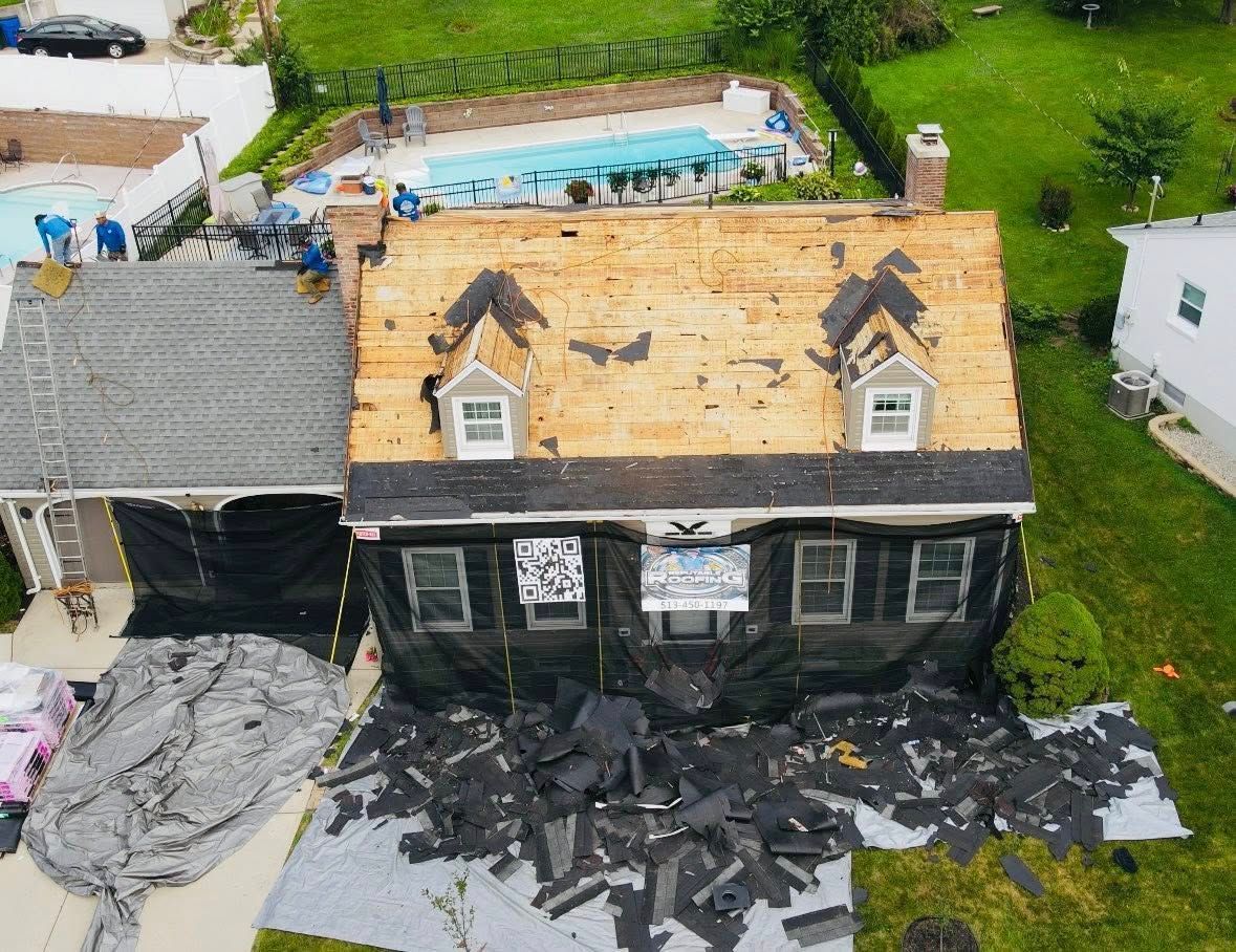 House roof replacement: workers on roof, old shingles removed, covered with black tarp, debris on ground.
