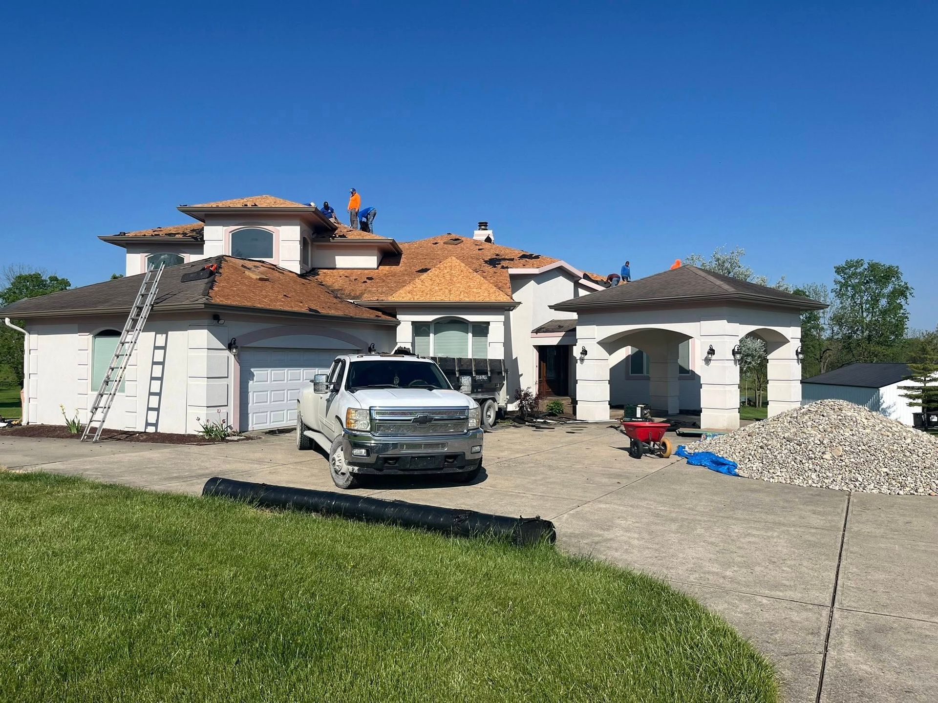 Roofers on a house with a damaged roof, a truck parked in front, and rock piles.