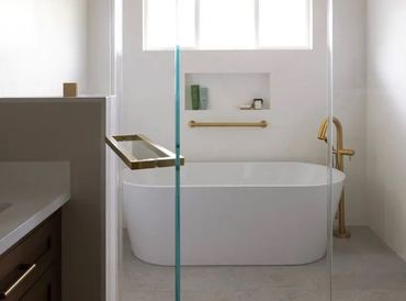 Modern bathroom with a freestanding tub, glass shower screen, and brass fixtures in a bright white space.