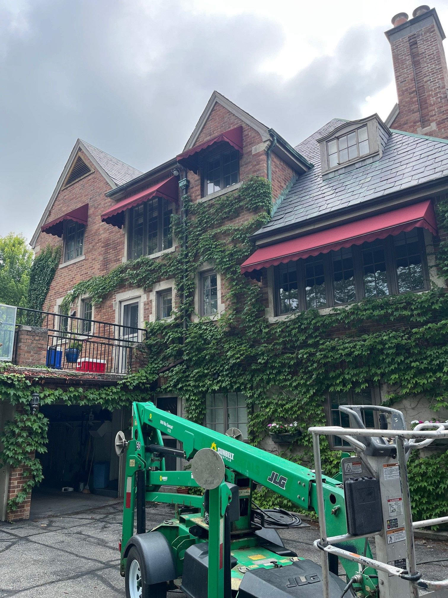 Brick house with ivy and red awnings behind a green construction lift in a courtyard