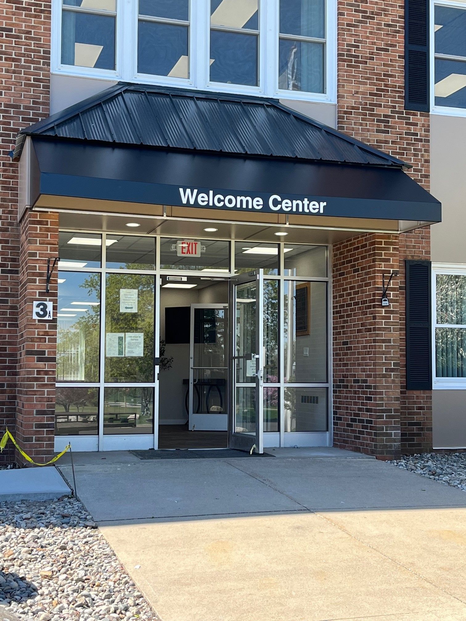 Brick building entrance with black awning labeled “Welcome Center” and glass double doors