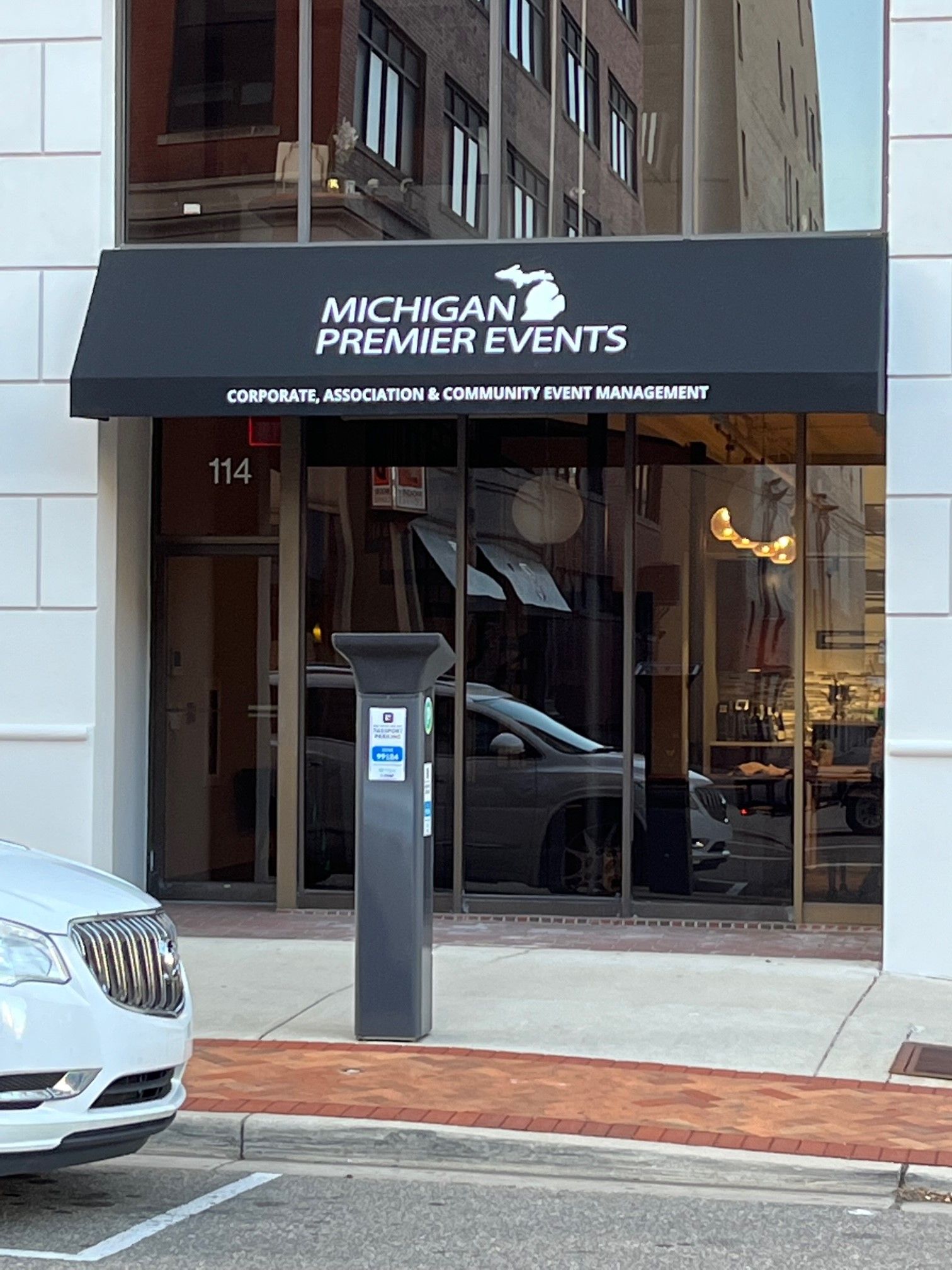 A white car is parked in front of a Michigan premier events building.