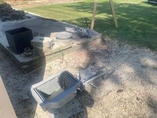 Damaged outdoor light fixture next to a concrete structure with debris, set on grass.