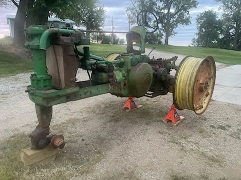 Old green and yellow John Deere tractor on jack stands outdoors.