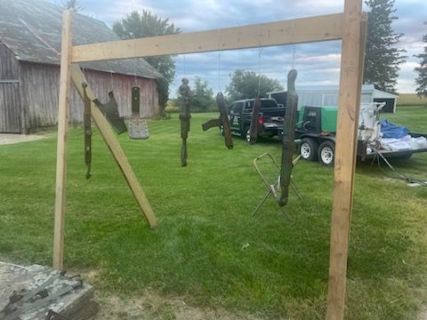 Wooden frame holding items hanging on strings outdoors; barn in background.