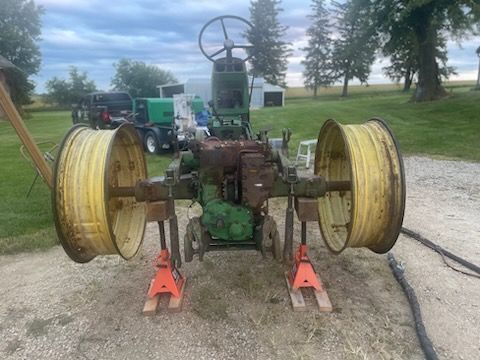 Green John Deere tractor on jack stands, large yellow wheels, outdoors.