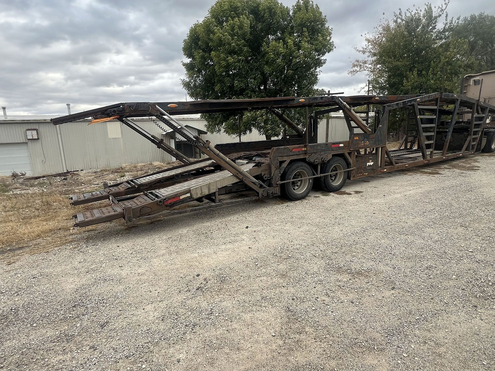 A long, black car hauler trailer parked on gravel.