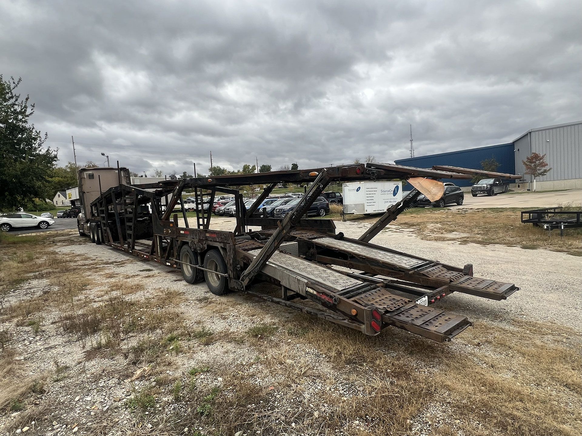 Burnt car hauler trailer in a gravel lot on an overcast day.