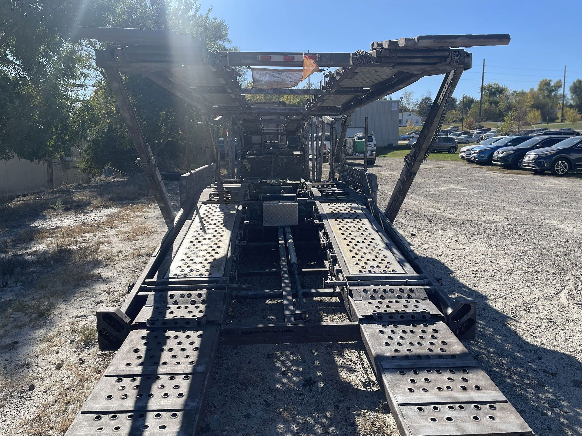 Car hauler trailer on a gravel lot under sunlight.