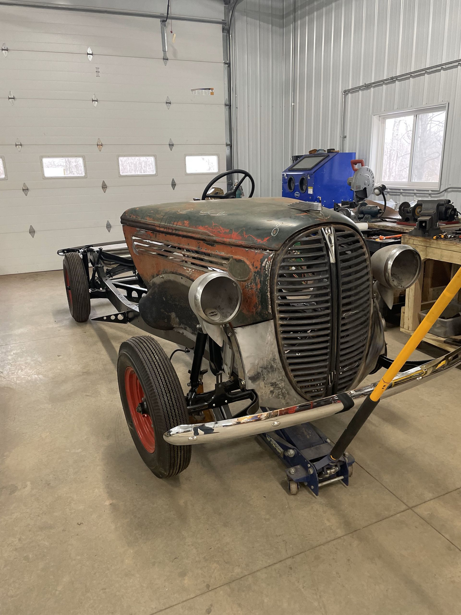 An old car is sitting on a jack in a garage.