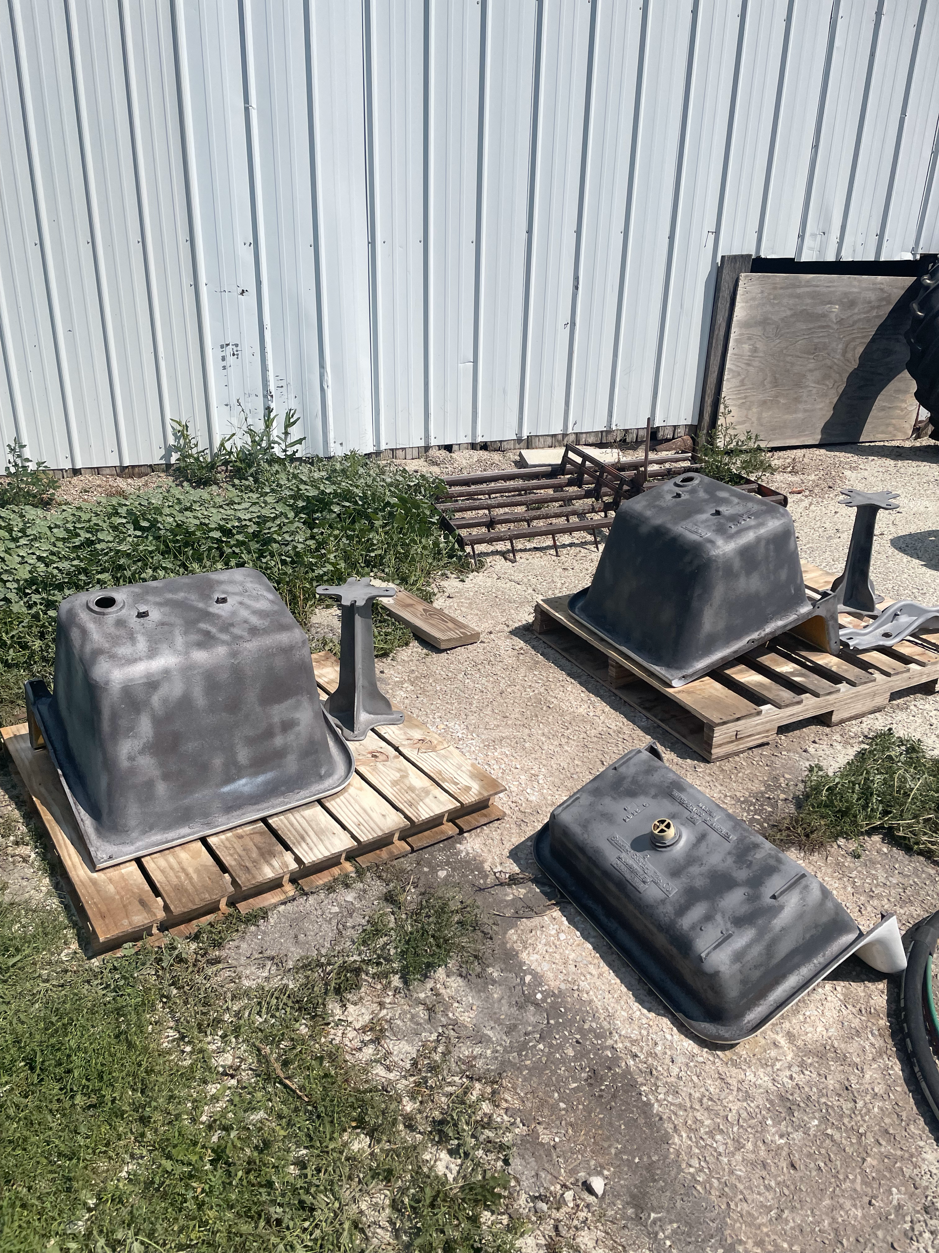 Three sinks are sitting on wooden pallets in a yard.