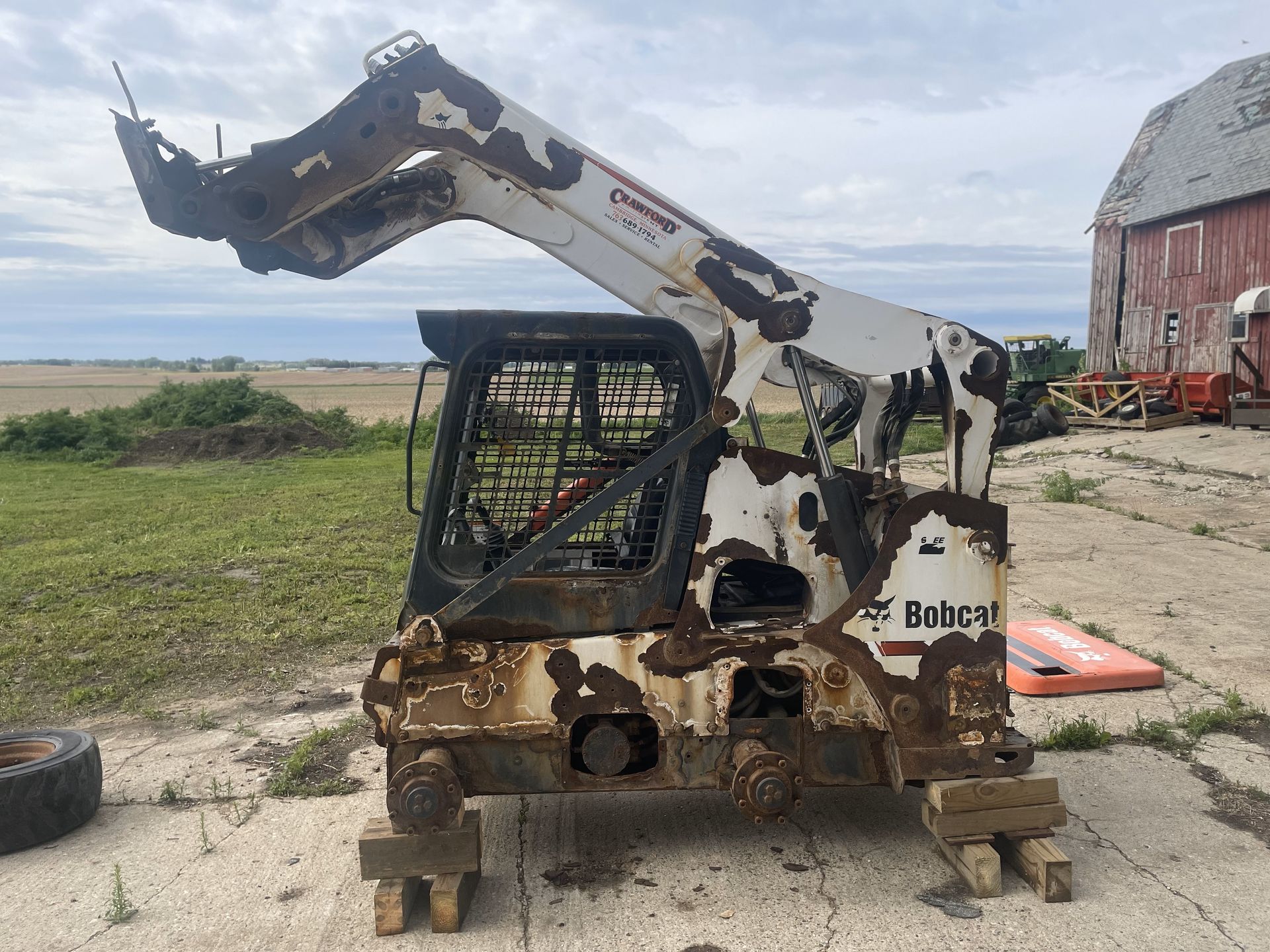A bobcat tractor is sitting in a field next to a barn.