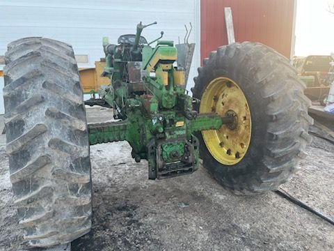 a green john deere tractor with large tires is parked in front of a garage